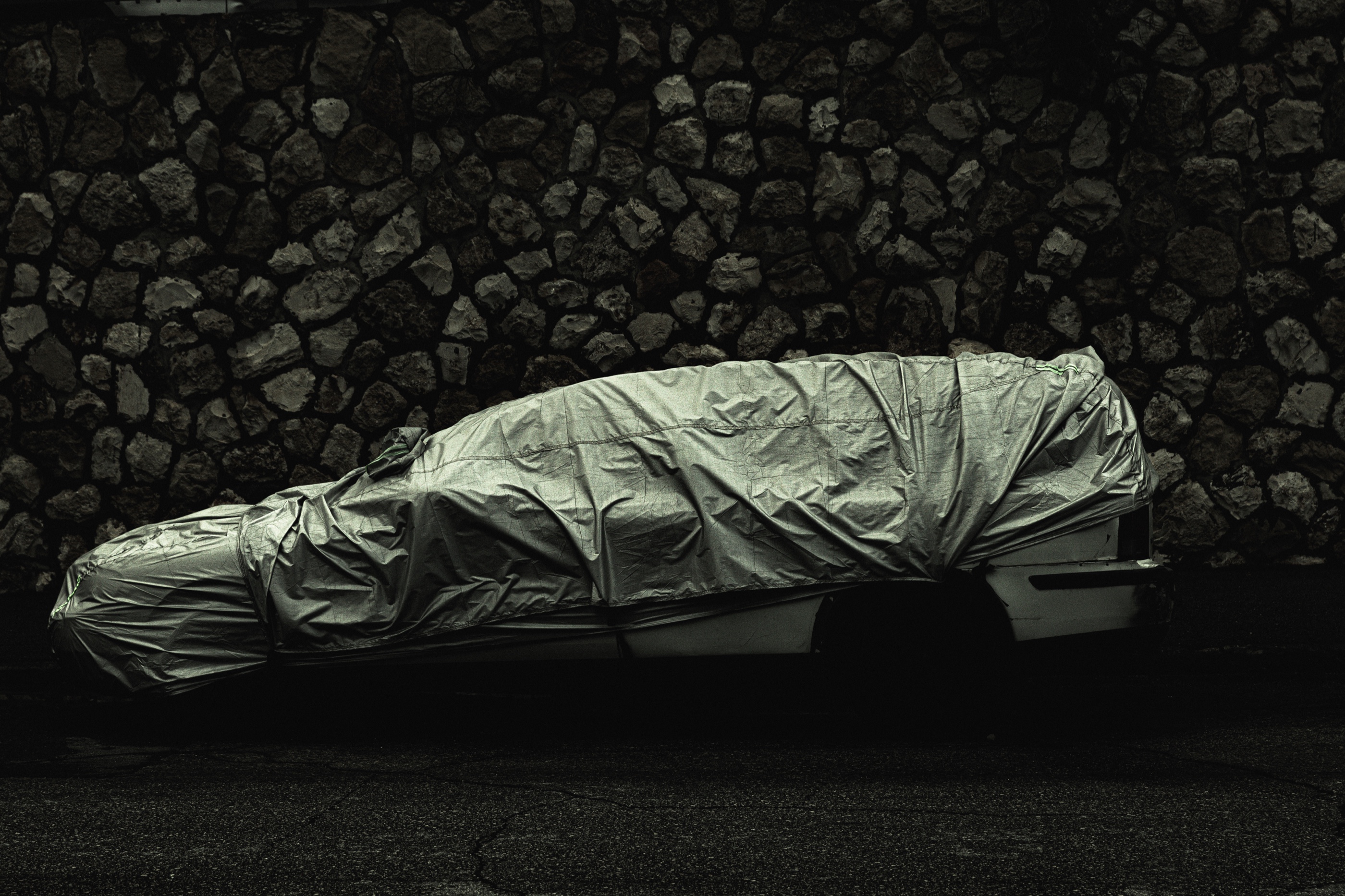 A covered car at night against a stone wall